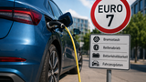 Elektroauto an einer Ladesäule neben einem Euro-7-Schild mit Hinweisen auf Bremsstaub, Reifenabrieb und Fahrzeugdaten.