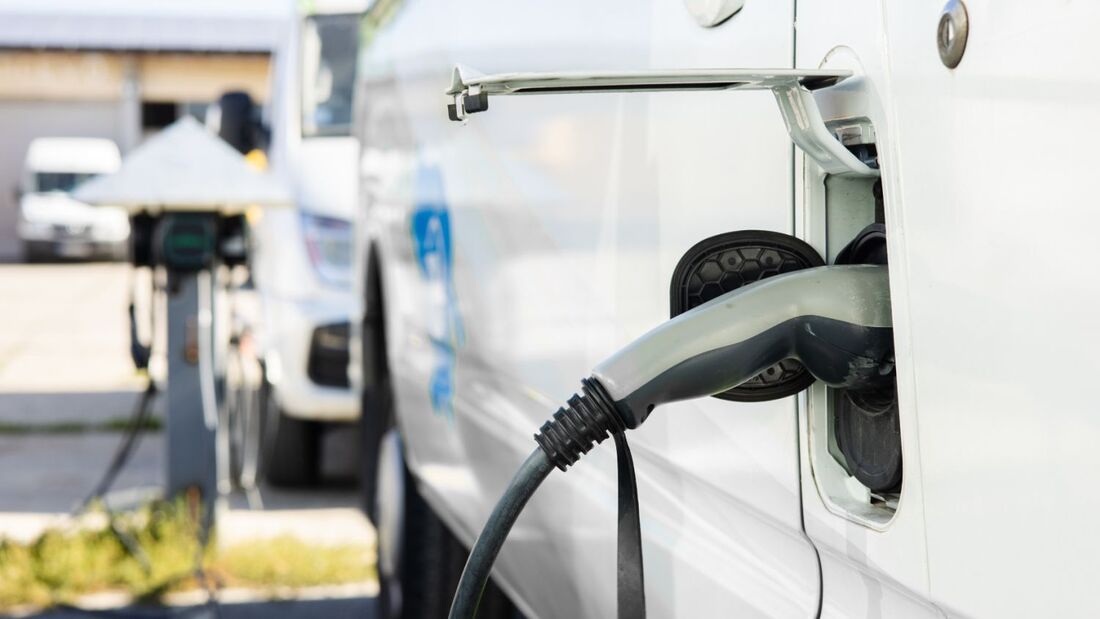 Elektrotransporter lädt an einer Ladestation auf Betriebsgelände, weiteres Nutzfahrzeug im Hintergrund.