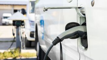 Elektrotransporter lädt an einer Ladestation auf Betriebsgelände, weiteres Nutzfahrzeug im Hintergrund.