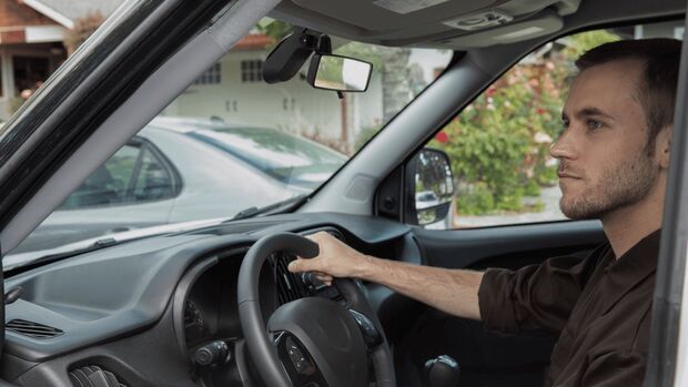 Fahrer sitzt am Steuer eines Fahrzeugs, Nauto-Dashcam an der Frontscheibe sichtbar, Innenraumaufnahme im Flotteneinsatz.