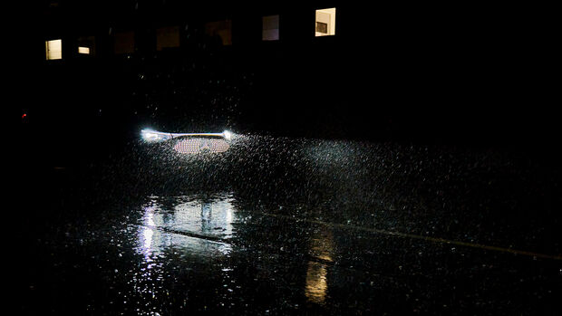 Fahrzeug fährt bei starkem Regen und Dunkelheit in einer Testumgebung mit nasser Fahrbahn und eingeschränkter Sicht