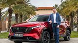 Felix Gebhart, Vertriebschef von Mazda Deutschland, steht neben einem roten Mazda CX-5 im Außenbereich.