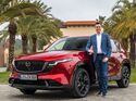 Felix Gebhart, Vertriebschef von Mazda Deutschland, steht neben einem roten Mazda CX-5 im Außenbereich.