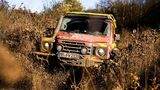 Feuerwehr-INEOS-Grenadier fährt frontal durch tiefen Schlamm und wirbelt große Schmutzmengen auf.