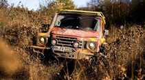 Feuerwehr-INEOS-Grenadier fährt frontal durch tiefen Schlamm und wirbelt große Schmutzmengen auf.