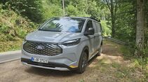 Ford E-Transit Custom AWD Trail in Frontansicht auf einem Waldparkplatz mit markantem Kühlergrill.