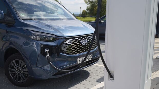 Ford E-Transit Custom an einer DC-Schnellladesäule, Ladekabel angeschlossen, Frontansicht des Fahrzeugs.