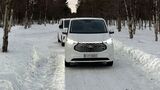 Ford E-Transit Custom beim Wintertest auf schneebedeckter Straße, Frontansicht des Fahrzeugs im Testbetrieb.