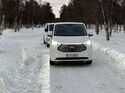 Ford E-Transit Custom beim Wintertest auf schneebedeckter Straße, Frontansicht des Fahrzeugs im Testbetrieb.