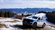 Ford Ranger Plug-in-Hybrid der Bergwacht Bayern auf verschneitem Alpenweg nahe einer Berghütte.