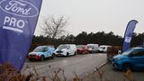 Ford Transit und Transit Custom als Fahrzeugreihe beim Ford Pro Leisure Experience Event in Lommel, mit Ford Pro Flaggen am Parkplatz.