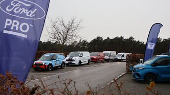 Ford Transit und Transit Custom als Fahrzeugreihe beim Ford Pro Leisure Experience Event in Lommel, mit Ford Pro Flaggen am Parkplatz.