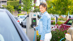 Frau hält Ladekabel an Mennekes AMTRON Wallbox auf einem Parkplatz im Freien neben einem Elektroauto.