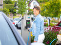 Frau hält Ladekabel an Mennekes AMTRON Wallbox auf einem Parkplatz im Freien neben einem Elektroauto.