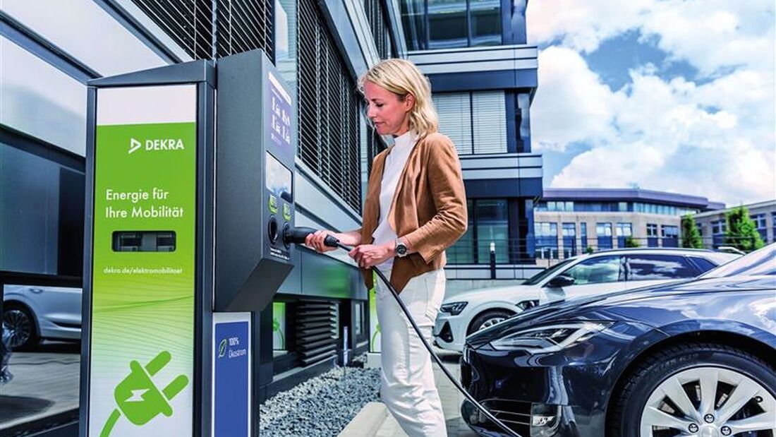 Frau lädt ein Elektroauto an einer DEKRA-Ladesäule vor einem Bürogebäude. 