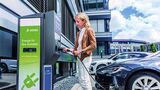Frau lädt ein Elektroauto an einer DEKRA-Ladesäule vor einem Bürogebäude.