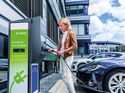 Frau lädt ein Elektroauto an einer DEKRA-Ladesäule vor einem Bürogebäude. 