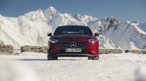 Frontansicht eines roten Mercedes CLA auf verschneiter Passstrasse vor Bergpanorama.