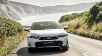 Frontansicht eines weißen Honda Civic e:HEV auf einer Küstenstraße vor Felsen und Meer.