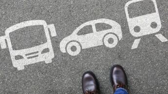 Füße auf Asphalt vor Symbolen für Bus, Auto und Zug als Darstellung verschiedener Verkehrsmitteloptionen.