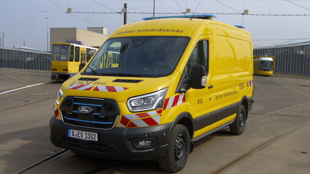 Gelber Ford E-Transit Custom der BVG auf einem Betriebshof mit Straßenbahnen im Hintergrund.