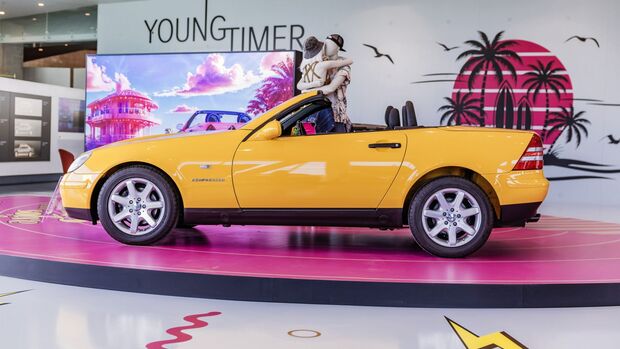Gelber Mercedes-Benz SLK Roadster in Seitenansicht auf Ausstellungsflaeche in Innenraum, Verdeck geoeffnet, vier Sitze sichtbar.