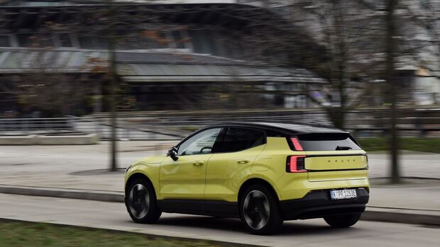 Gelber Volvo EX30 P8 AWD Electric bei einer Fahraufnahme schräg von hinten mit eingeschalteten Rückleuchten.