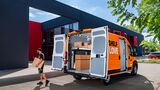 Geöffneter Sixt-van&truck-Transporter mit Sortimo-Regalsystem, ein Zusteller trägt ein Paket zum Fahrzeug.