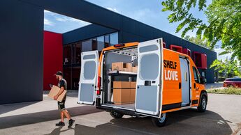 Geöffneter Sixt-van&truck-Transporter mit Sortimo-Regalsystem, ein Zusteller trägt ein Paket zum Fahrzeug.