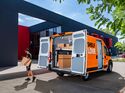 Geöffneter Sixt-van&truck-Transporter mit Sortimo-Regalsystem, ein Zusteller trägt ein Paket zum Fahrzeug.