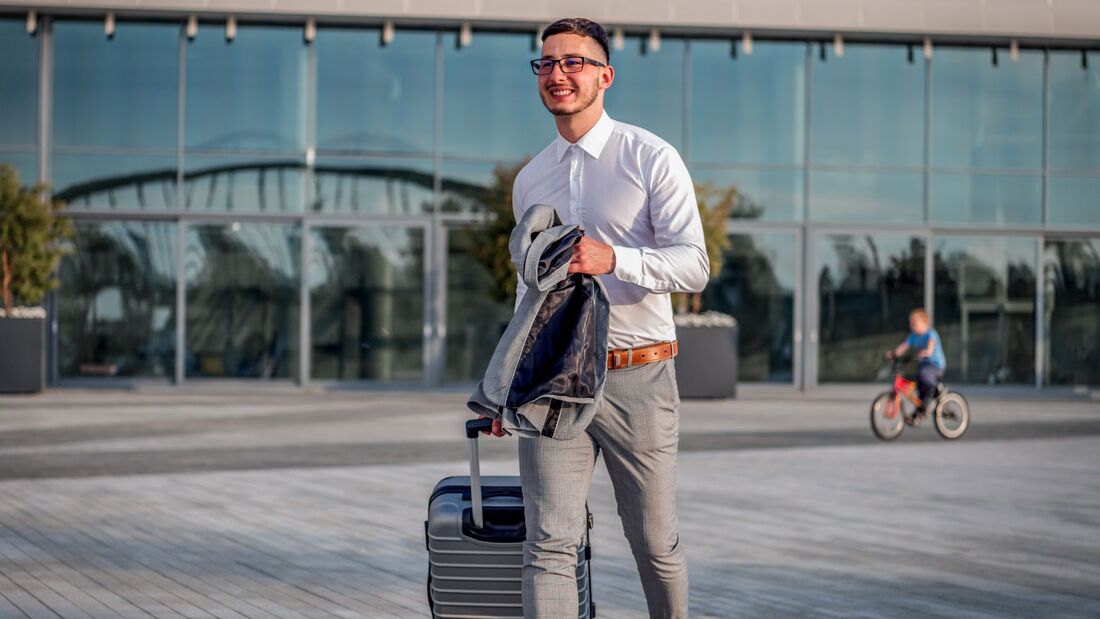 Geschäftsreisender mit Rollkoffer vor einem Bürogebäude – Symbolbild zur Studie über KI, Kosten und Geschäftsmobilität 2026.