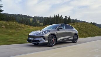Grauer MG IM6 in Seiten- und Frontansicht während der Fahrt auf einer Straße in einer bewaldeten Hügellandschaft.