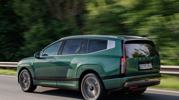 Grüner Hyundai Ioniq 9 Elektro-SUV in Seitenansicht während der Fahrt auf einer Straße mit unscharfem Waldhintergrund.