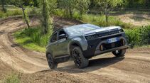 Grüner Jeep Avenger 4xe fährt auf einem unbefestigten Offroad-Parcours über eine Bodenwelle.