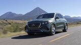 Grüner Mercedes-Benz GLE 450e 4MATIC in schräger Frontansicht auf einer Landstraße vor einer Berglandschaft bei Sonnenschein.