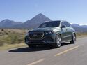 Grüner Mercedes-Benz GLE 450e 4MATIC in schräger Frontansicht auf einer Landstraße vor einer Berglandschaft bei Sonnenschein.