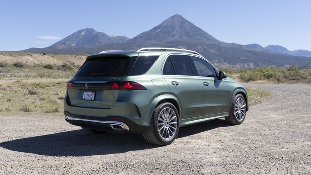 Grüner Mercedes-Benz GLE 450e 4MATIC in schräger Heckansicht auf einem Schotterplatz mit Rückleuchten, Dachreling und Leichtmetallrädern.