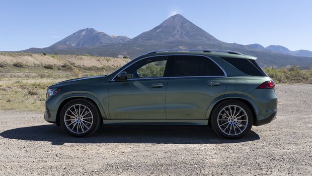 Grüner Mercedes-Benz GLE 450e 4MATIC in vollständiger Seitenansicht auf einem Schotterplatz vor einer Berglandschaft.