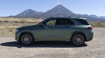 Grüner Mercedes-Benz GLE 450e 4MATIC in vollständiger Seitenansicht auf einem Schotterplatz vor einer Berglandschaft.