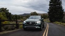 Grüner Mercedes-Benz GLE 450e 4MATIC mit eingeschalteten LED-Scheinwerfern auf einer kurvigen Landstraße zwischen Bäumen.