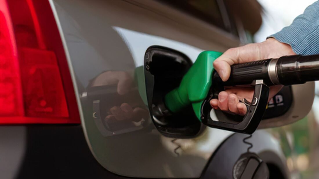 Hand steckt eine grüne Benzin-Zapfpistole in den Tankstutzen eines silbernen Autos, Nahaufnahme an einer Tankstelle