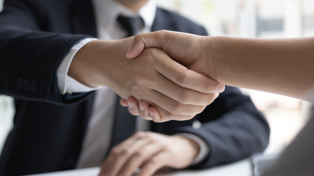 Handschlag zwischen Mann im dunklen Anzug und Gegenüber am Schreibtisch mit Unterlagen – Symbolbild für Jobs im Fuhrpark- und Mobilitätsmanagement