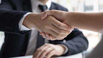 Handschlag zwischen Mann im dunklen Anzug und Gegenüber am Schreibtisch mit Unterlagen – Symbolbild für Jobs im Fuhrpark- und Mobilitätsmanagement