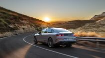 Heckansicht der vollelektrischen Mercedes C-Klasse auf einer Landstraße bei Sonnenuntergang.