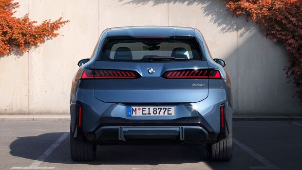 Heckansicht des BMW iX3 der Neuen Klasse vor einer Betonwand mit Herbstbewuchs.