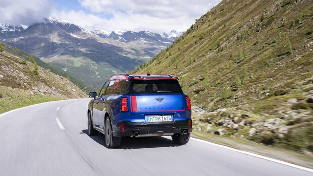 Heckansicht des MINI Countryman JCW auf einer Alpenstraße vor Bergpanorama.