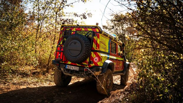 Heckansicht eines Feuerwehr-INEOS-Grenadier auf einem schmalen, matschigen Waldweg zwischen dichtem Bewuchs.