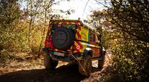 Heckansicht eines Feuerwehr-INEOS-Grenadier auf einem schmalen, matschigen Waldweg zwischen dichtem Bewuchs.
