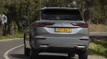 Heckansicht eines Mitsubishi Outlander Plug-in-Hybrid auf einer kurvigen Straße.