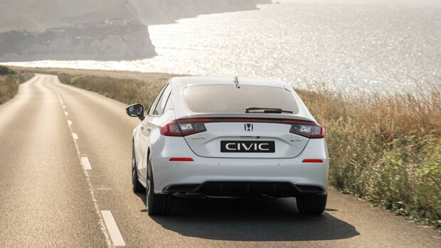 Heckansicht eines weißen Honda Civic e:HEV auf einer Küstenstraße mit Meer im Hintergrund.